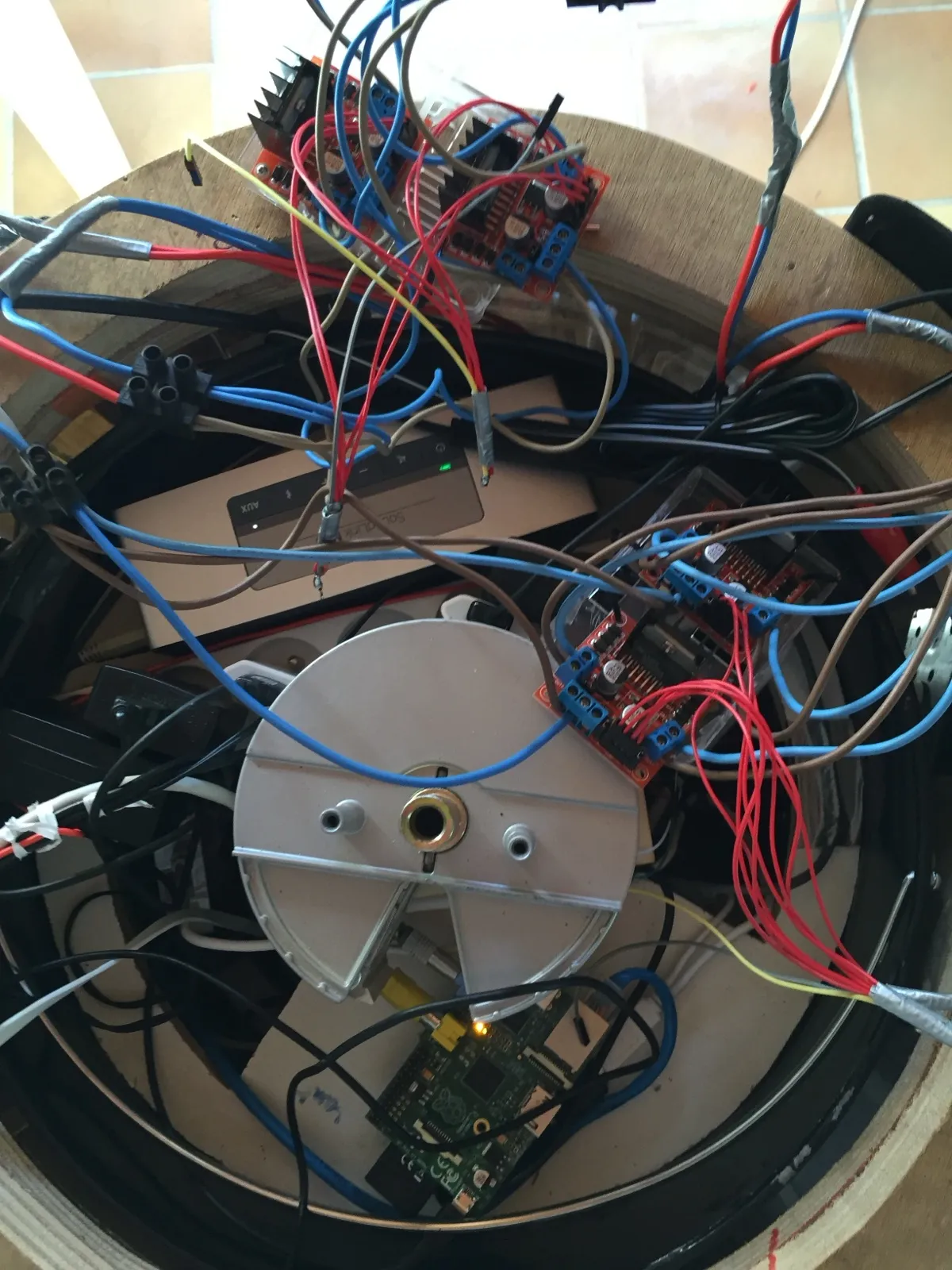 Vue du dessus de l’intérieur circulaire du robot : une carte Raspberry Pi verte, plusieurs modules L298N rouges, un disque métallique central et de nombreux câbles.