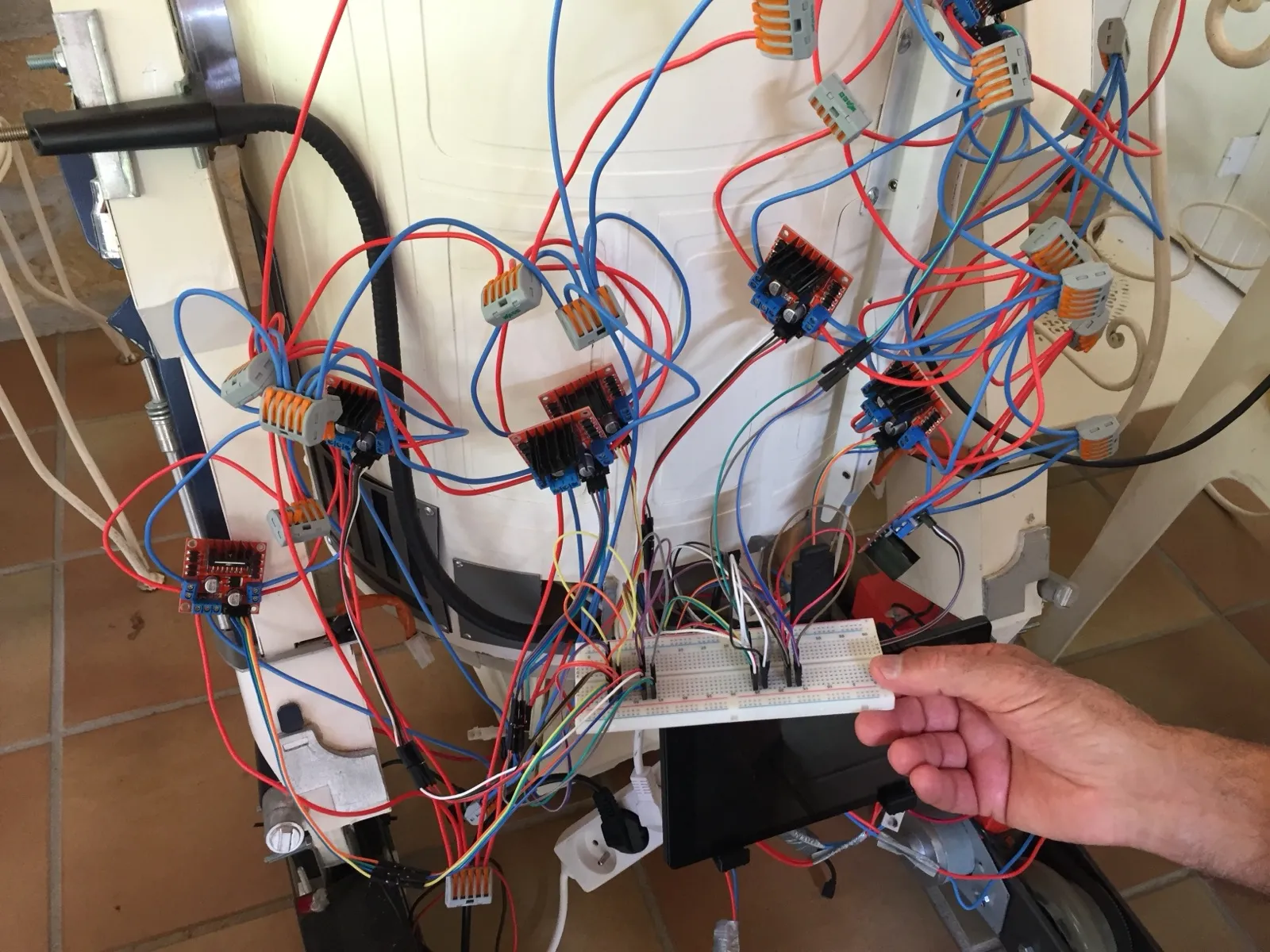 Intérieur du corps du robot : une dizaine de cartes contrôleurs à dissipateur noir, des bornes de connexion, une platine d’essai, et un faisceau dense de fils rouges et bleus.